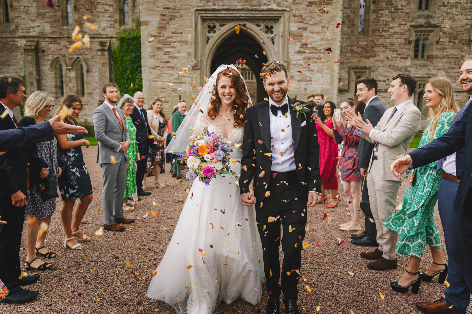 bride and groom covered in confetti thrown by guests at Hampton Court Castle